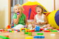 Toddlers sitting on the floor and laughing while playing with toys. 