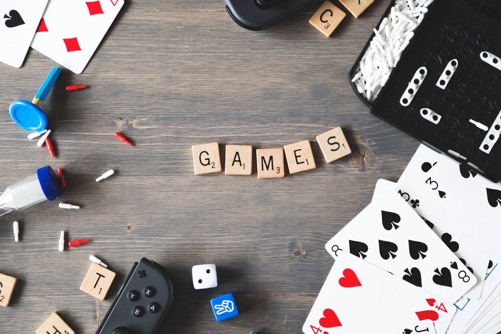 Cubulețe cu litere formând cuvântul 'GAMES', înconjurate de cărți de joc, zaruri și alte accesorii de joc pe un fundal din lemn.