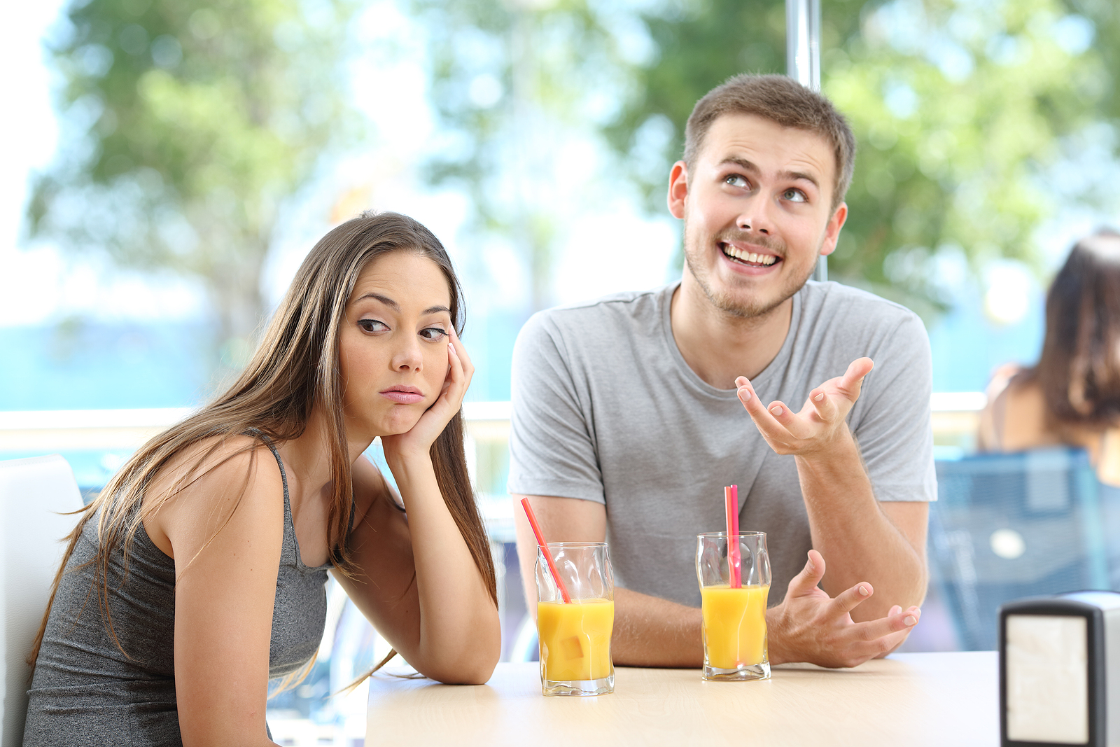 A young woman on a first date with a man looks annoyed to the side as he talks to her excitedly.