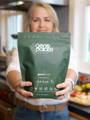 Person preparing a post-workout drink using GenoBlend protein and fiber powder in a modern kitchen.