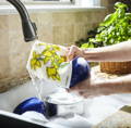 A person washes a blue bowl in the sink using a Swedish dishcloth with yellow flowers on it