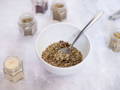 A white ceramic bowl and silver spoon filled with mixed spices, with open spice jars surrounding the bowl