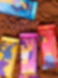 Four vibrant Fancis chocolate packages (Milk Chocolate, Merry Mango, Rich Chocolate, and Fruit & Nut) on a cocoa powder surface with scattered cocoa beans.