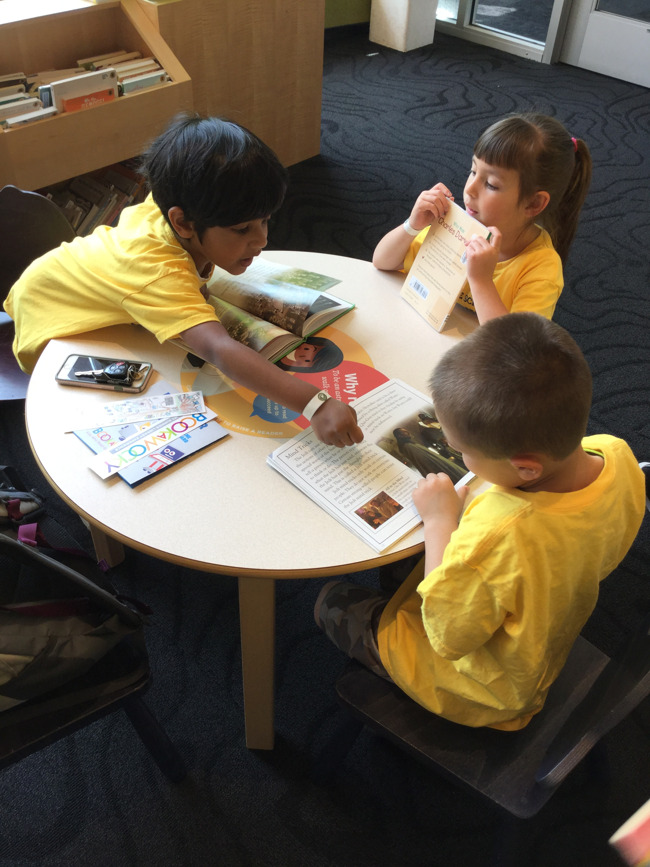 Young Primrose students helps his classmate with a book at the Rosemount library as their classmate looks on