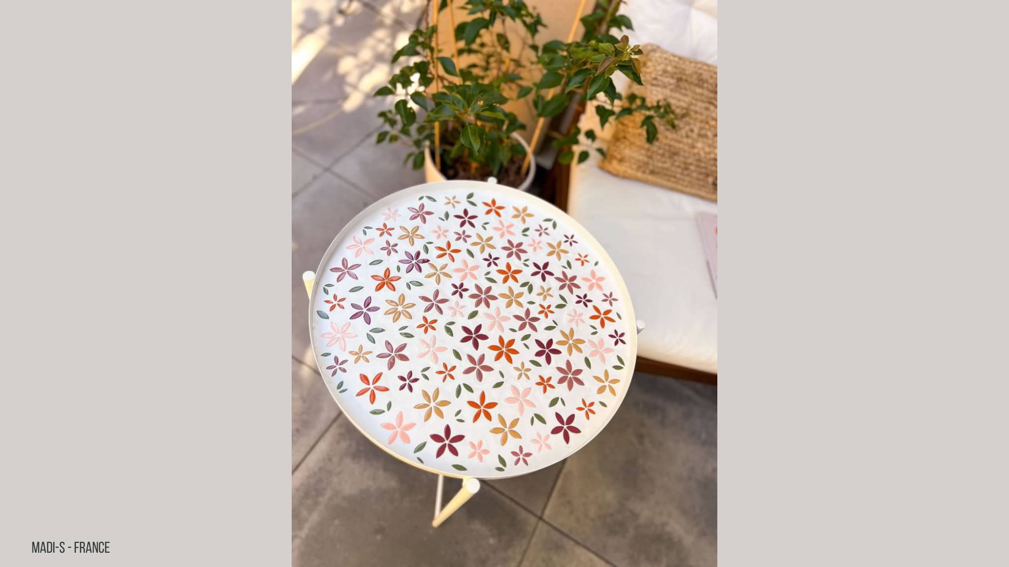 Rond tafeltje gemozaïekt met bloemblaadjes in verschillende kleuren met een witte voeg.