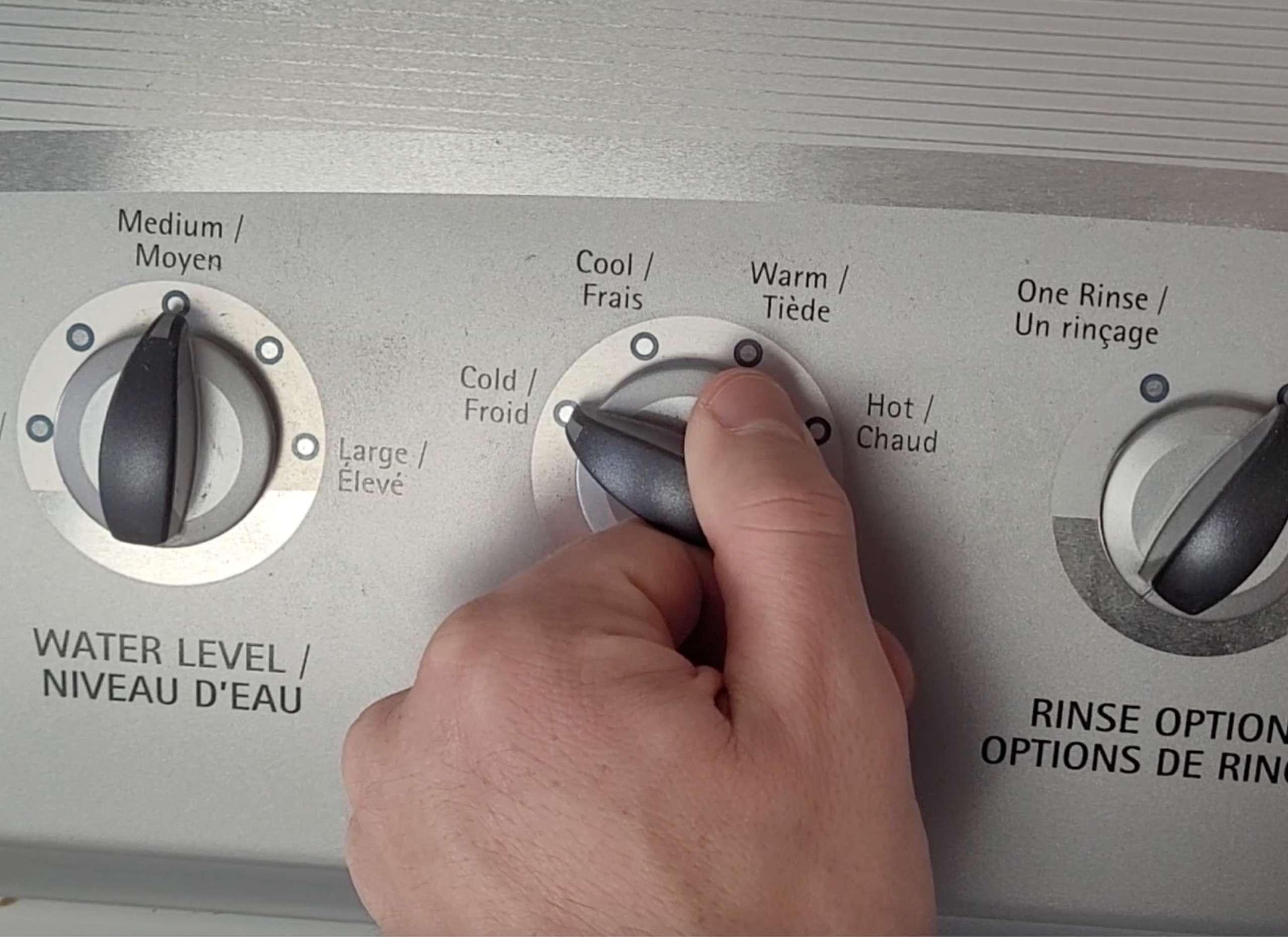 photo of a hand turning the dial on a washing machine to the cold water setting