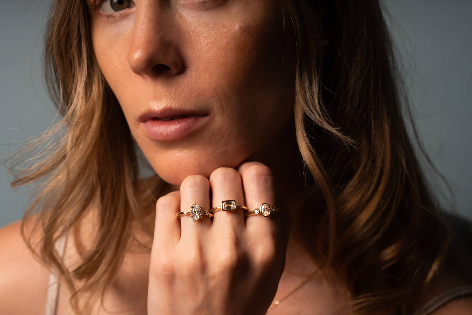 Model wearing three different diamond engagement rings on her fingers, showcasing various styles and cuts.