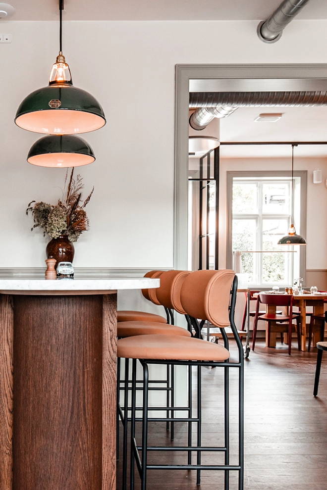 Large Green Coolicon Lampshades above tall bar-style restaurant table with orange leather bar stools.