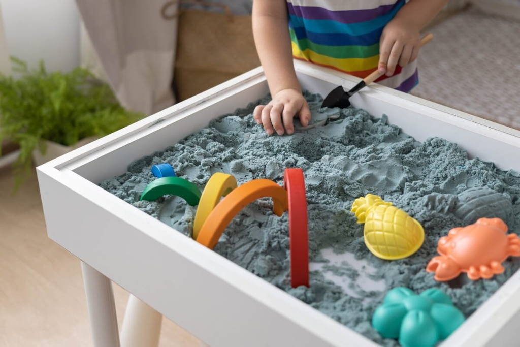 Toddler playing with blue sand inside a cute sensory table.