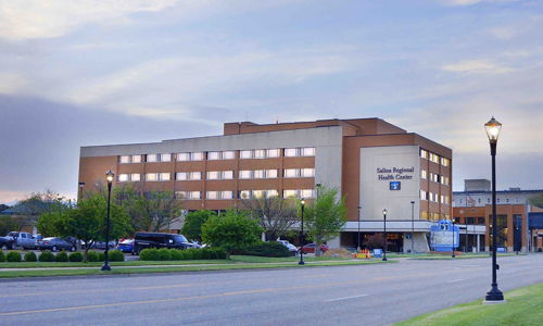 Well-maintained hospital building by a tree-lined road under an overcast sky, evoking safety, care, and community.