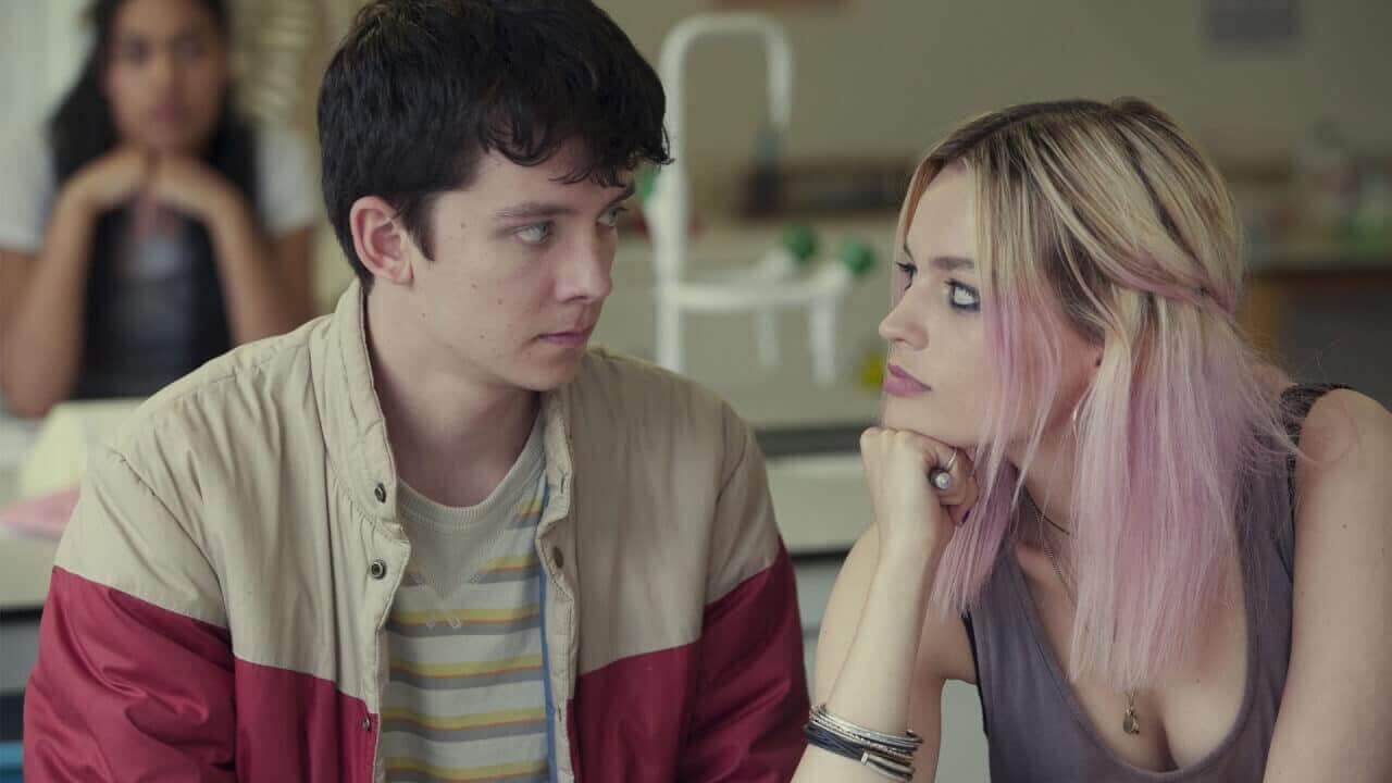 Otis and Maeve looking at eachother intently during a chemistry class. Meave has her hand on her chin.