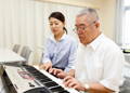 An adult male playing the electric guitar and reading tablature with the help of his private instructor.