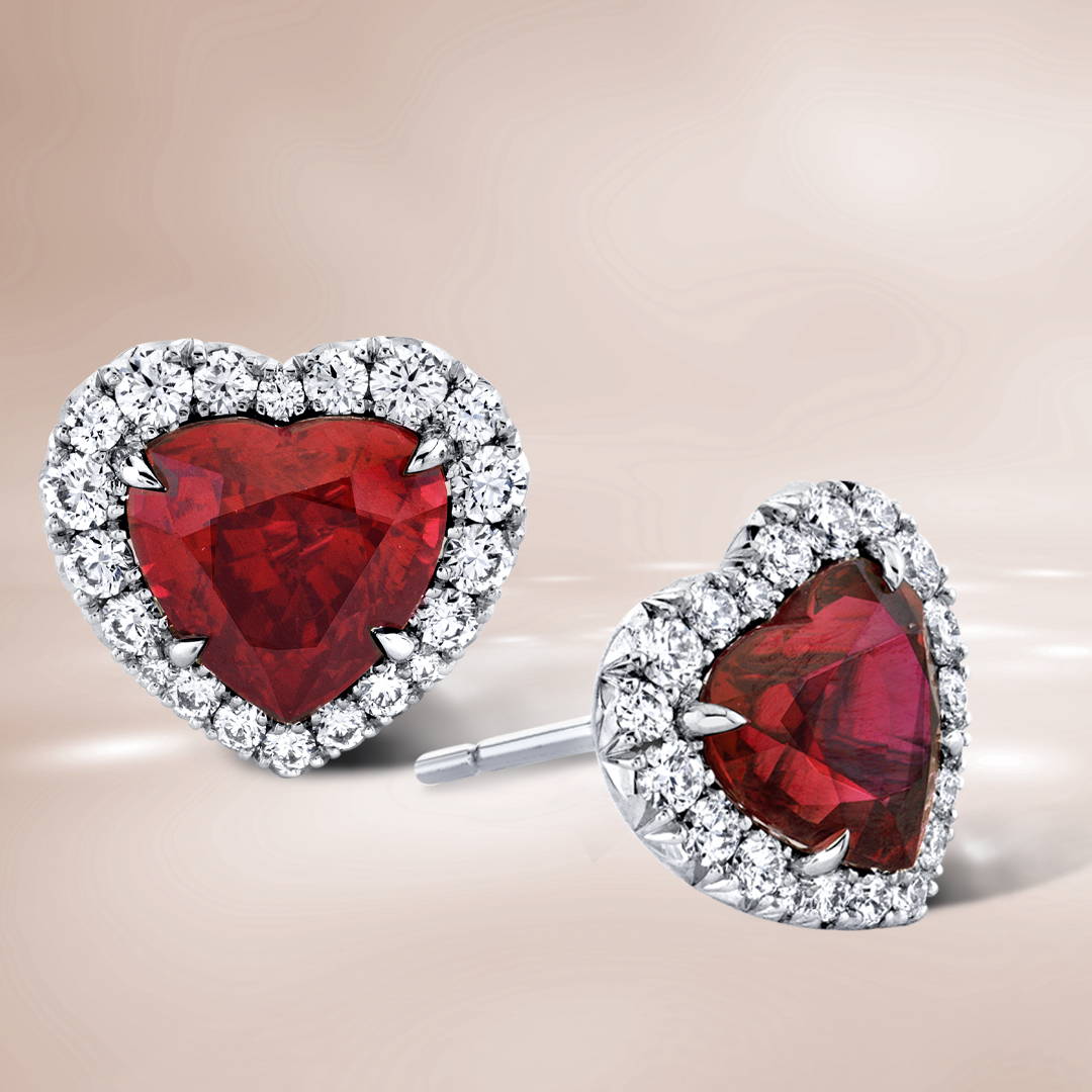 Heart shaped ruby stud earrings with diamond halo on a brown background