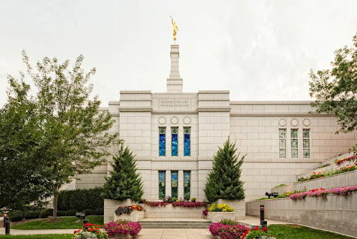Winter Quarters Temple standing and flower beds against a white, cloudy sky. 