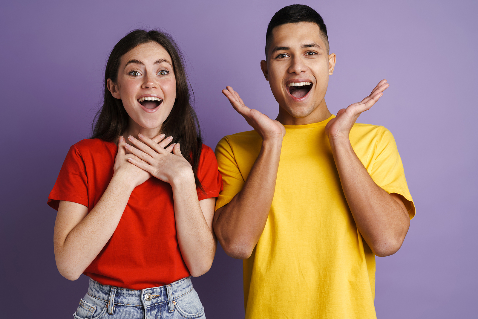 Brunette excited couple exclaiming and gesturing at camera isolated over purple wall.