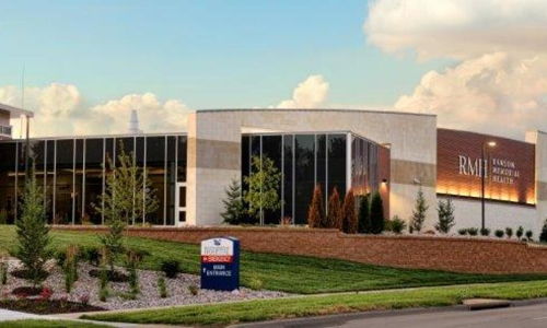 Modern building with glass windows, manicured landscaping, and a bright sky, evoking professionalism and calmness.