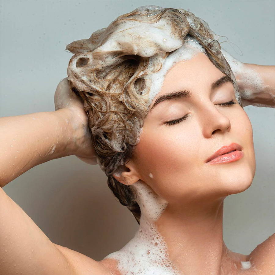woman with blonde hair and eye closed shampooing her hair