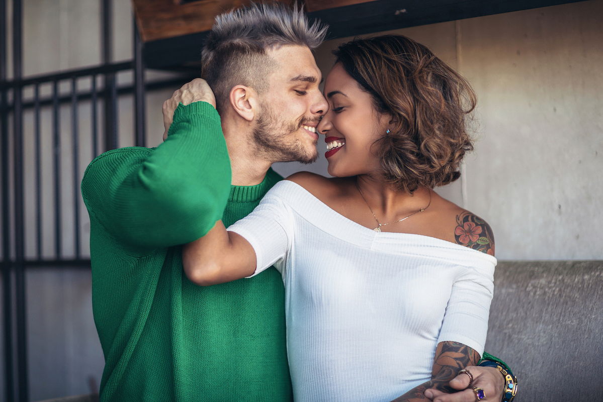 An attractive multi racial couple shares an intimate moment. They are smiling with their faces next to one another.