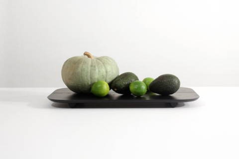 A green pumpkin, two avocados, and three limes on top of a black plate