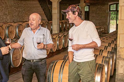 Bruno Laporte, le propriétaire du Château du Cauze, et David Madray, le maître de chai, se tiennent côte à côte dans le chai du domaine. Autour d'eux, on aperçoit les rangées impeccablement alignées de barriques en bois, témoignant du soin apporté à l'élevage des vins. 