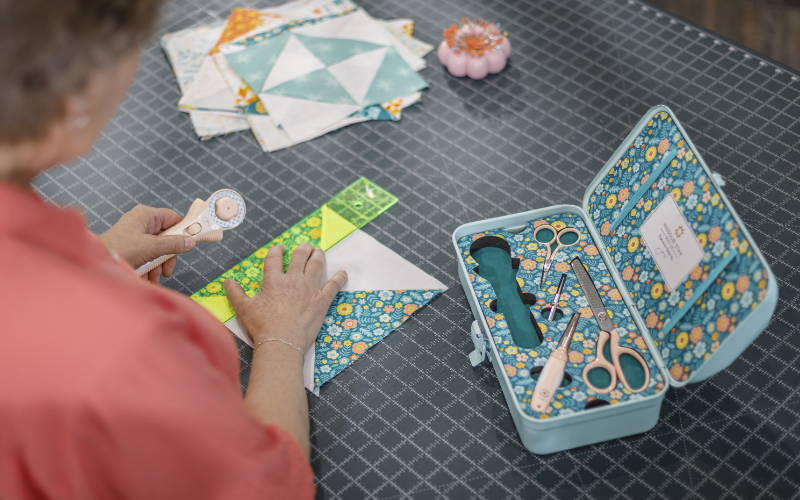 Jenny doan cutting a quilt block with her signature quilting toolbox nearby.