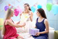 Pregnant woman opening baby shower gifts with friends