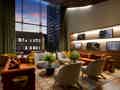 Stilvolle Hotellobby mit orangefarbenen Sofas, Pflanzen und großen Fenstern mit Blick auf die abendliche Skyline.