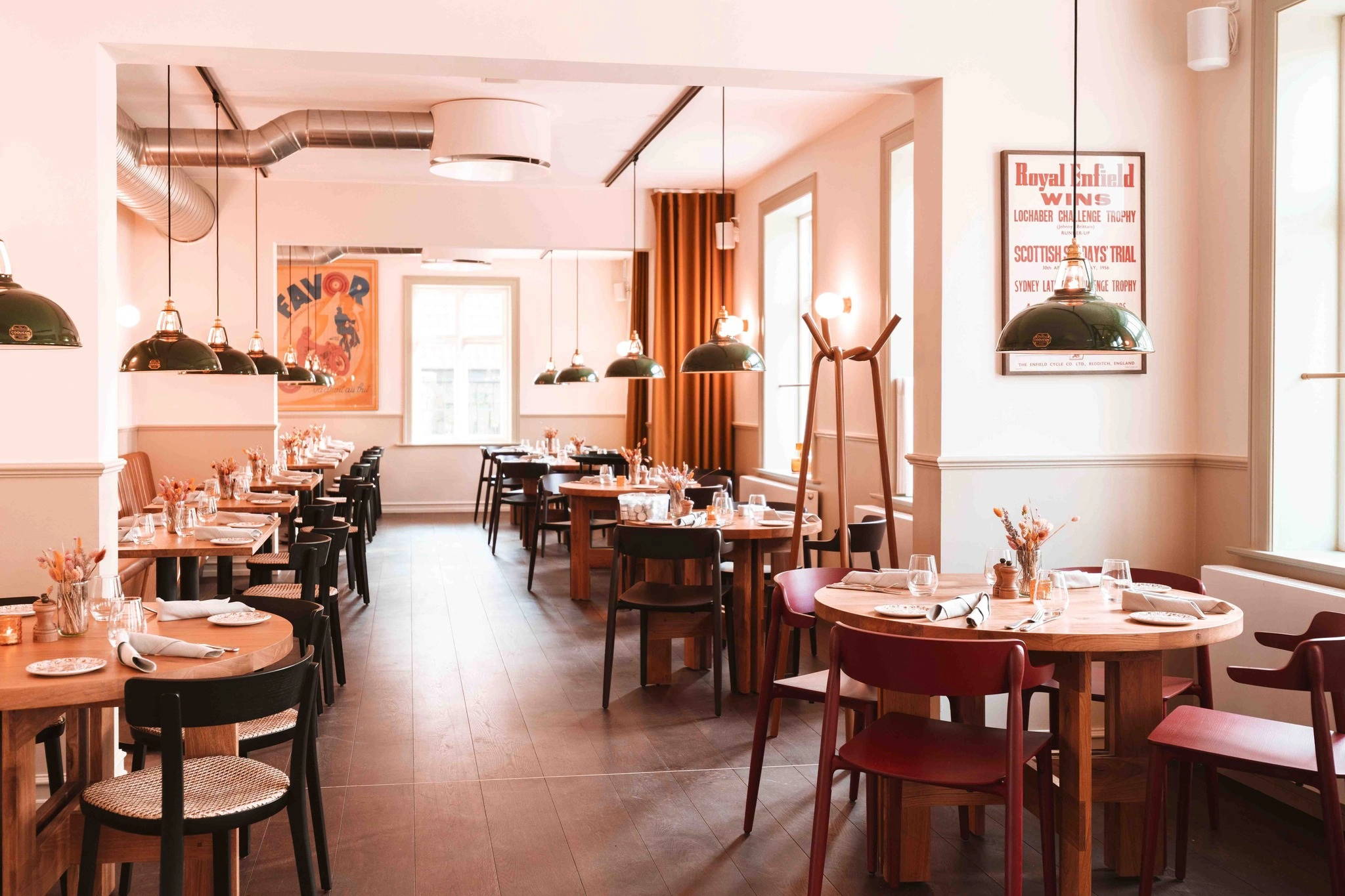 Looking down a Scandinavian restaurant at two rows of tables with Large Green Coolicon lampshades hanging above each one. 