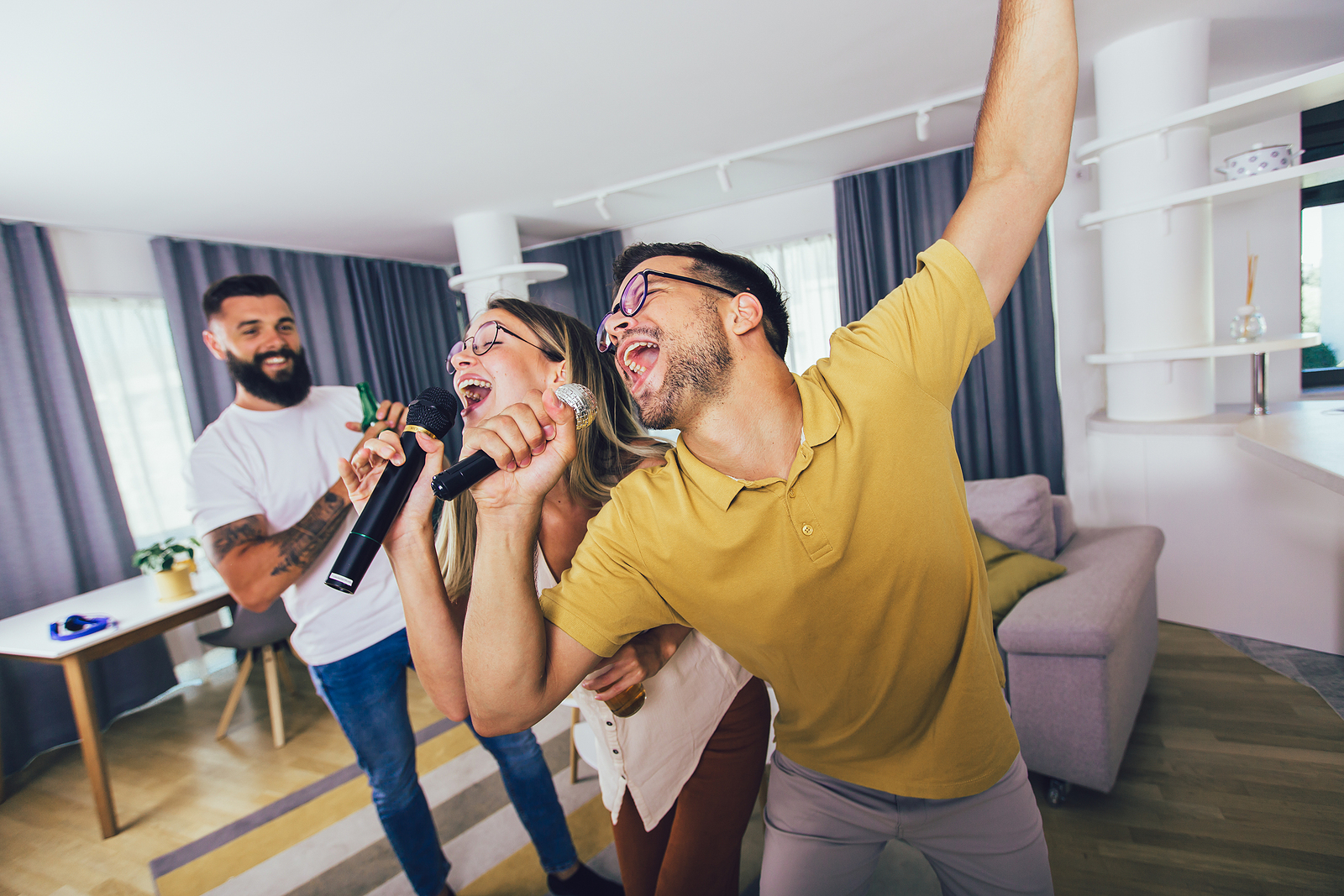 Two close friends sing together during a home karaoke get together while a friend looks on and smiles.