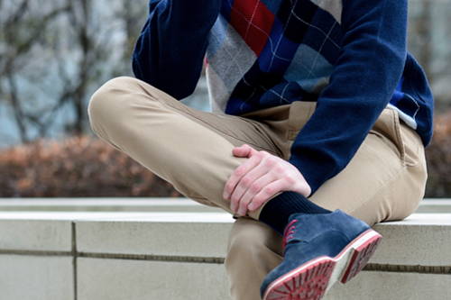 A young man sitting on a ledge grasping his leg while wearing compression socks