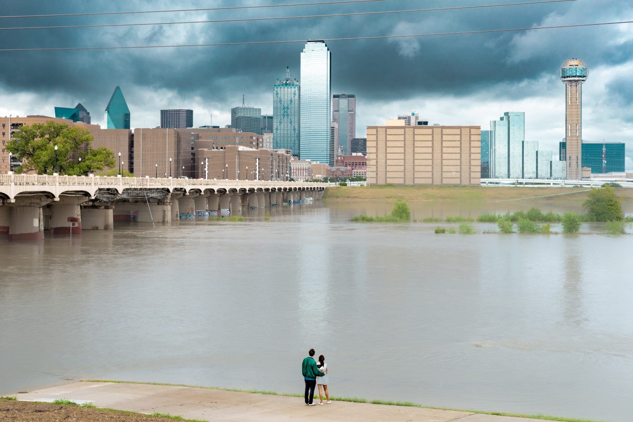 Trinity River filled with water up to the levees on August 22, 2022. A couple strolls by and looks out across water. Photo by Hexel Colorado.