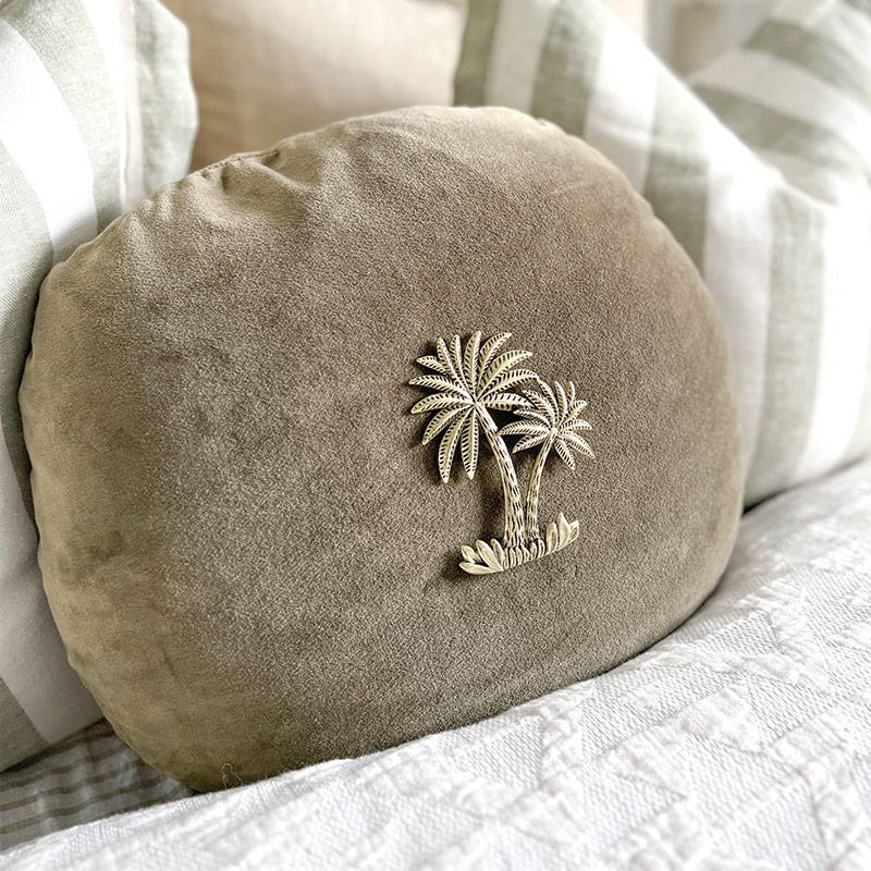 A palm tree cushion on a round cushion that is used an accent cushion on a bed.