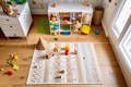 Beautiful Montessori-inspired playroom with shelves, cupboards, a carpet and lots of toy laying around. 