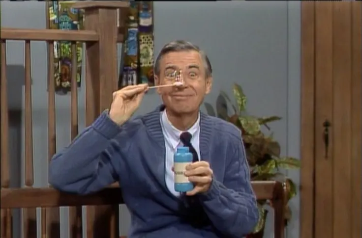 Mr Rogers smiling looking through a small bubble made by a soap and wand.