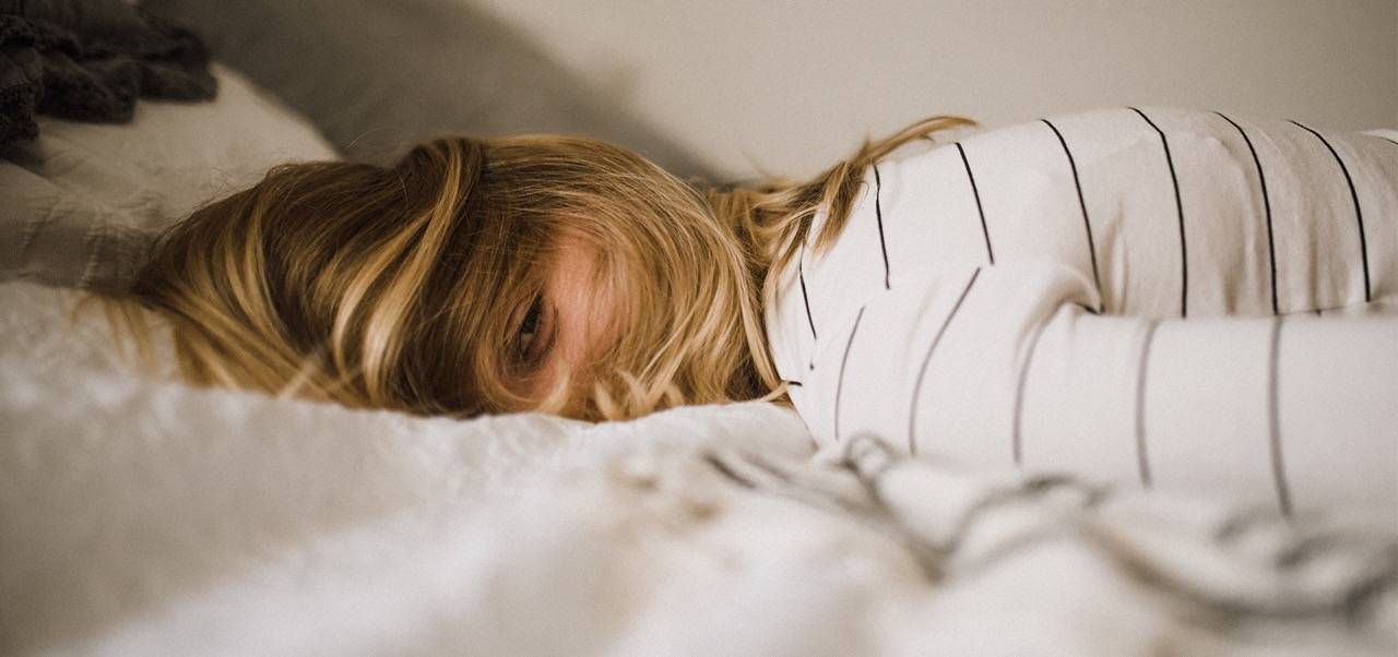 Frau liegt mit blonden Haaren vorm Gesicht auf einem Bett