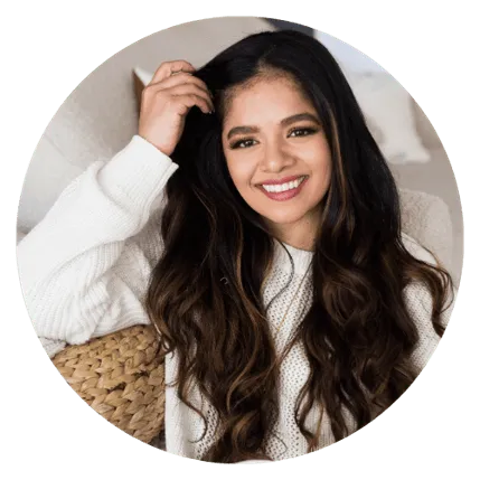 Smiling woman with long dark hair in cozy white sweater, sitting with a woven basket behind her.