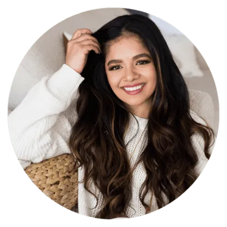 Smiling woman with long dark hair in cozy white sweater, sitting with a woven basket behind her.