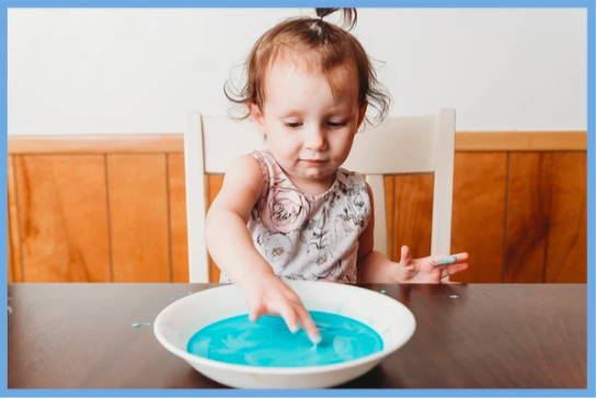 Toddler making hands messy in oobleck.