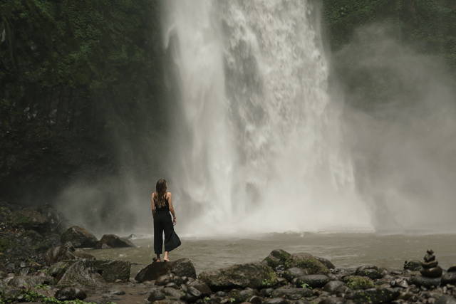 Small aperture: woman pauses at foot of waterfall