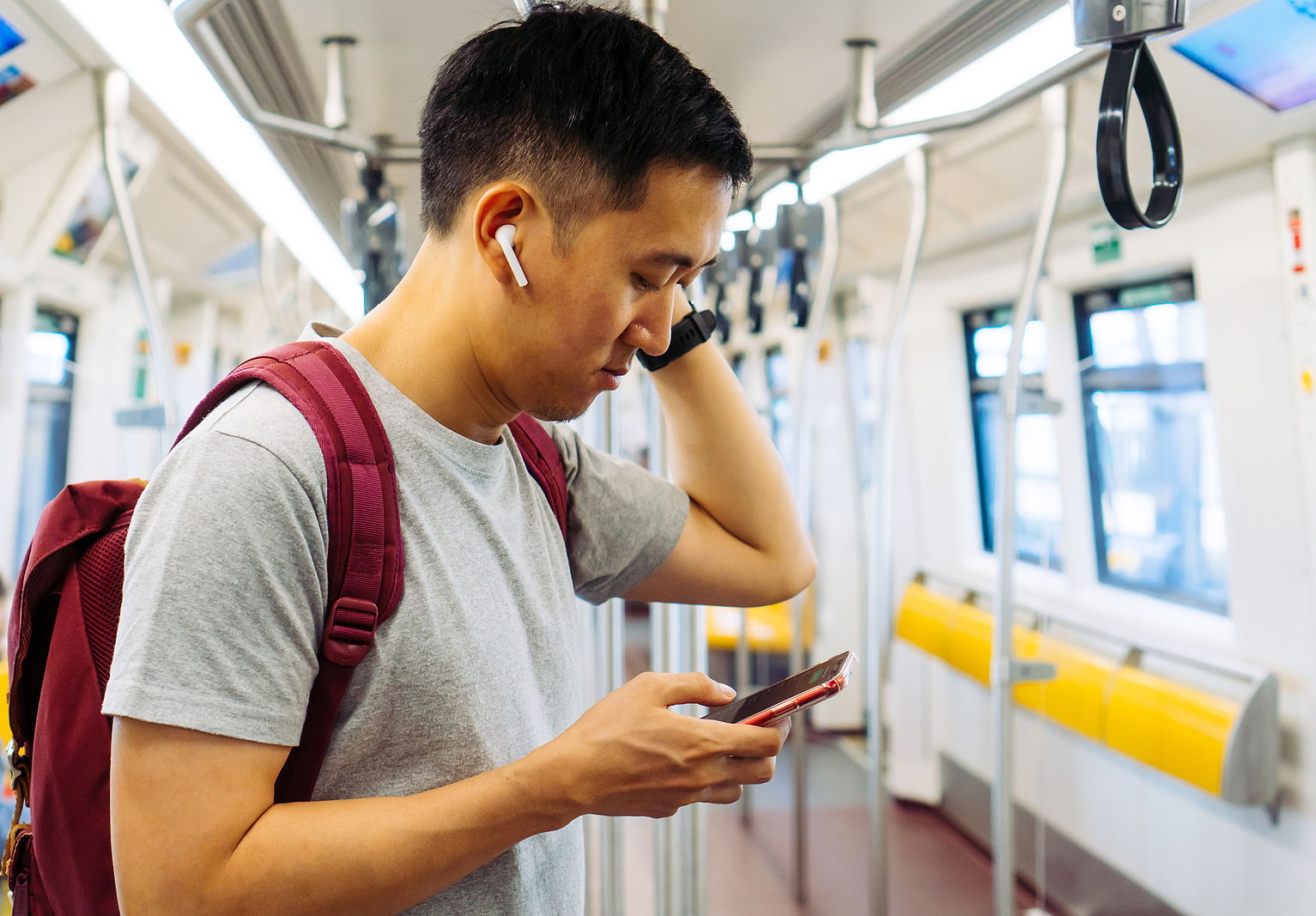 An asian man looks down on his phone while riding the subway and with headphones.