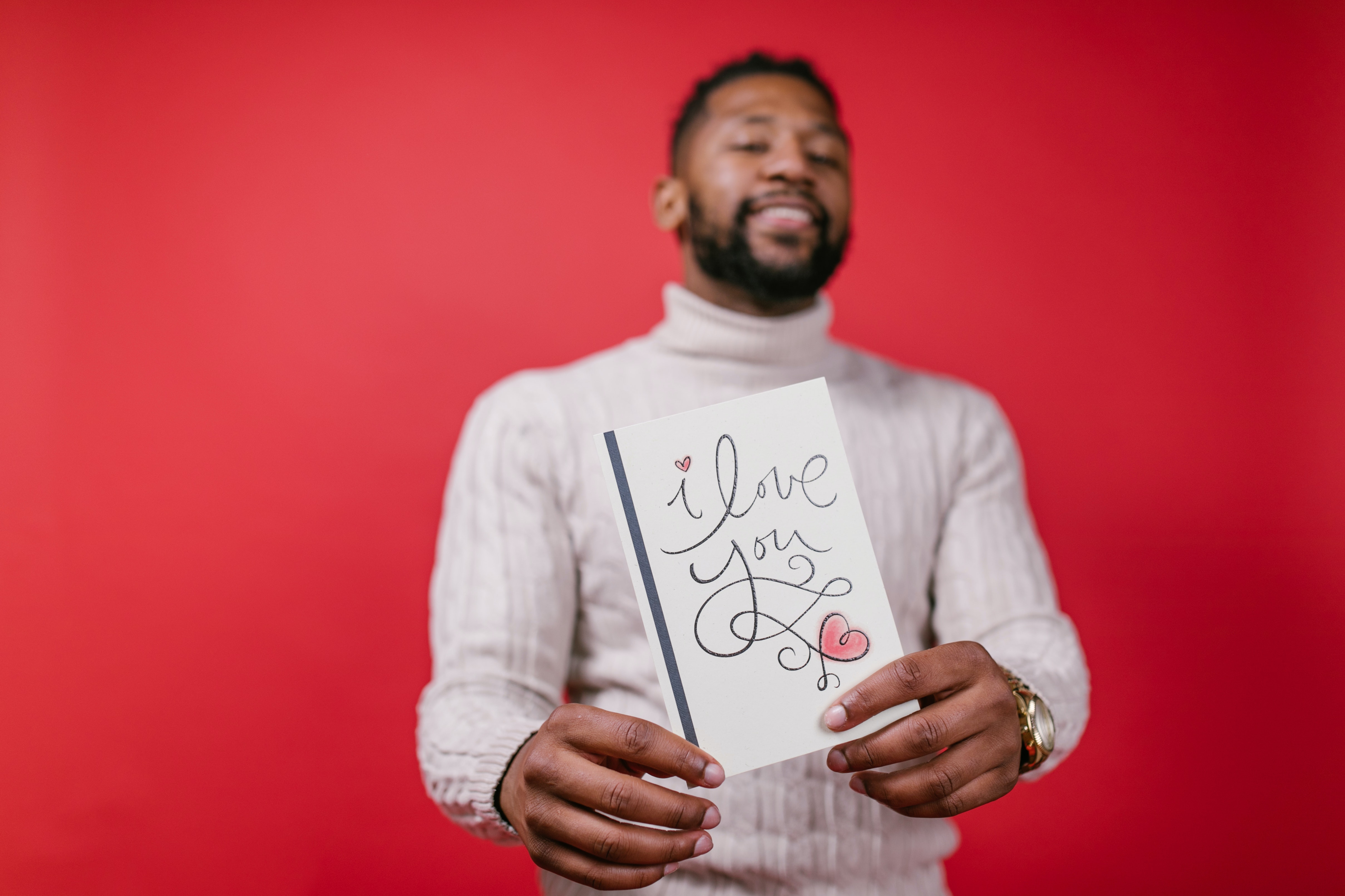 An attractive black man wearing a turtle neck with a valentines card with the words I love you with a heart at the bottom