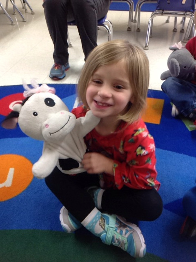 Young student smiles as she plays with Molly the cow hand puppet