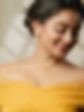 Smiling woman wearing an elegant gold necklace and matching earrings, captured in a warm, softly lit setting.