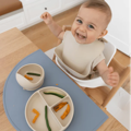 Little baby sitting at the table and eating from the Montessori First Bites Gift Set. 