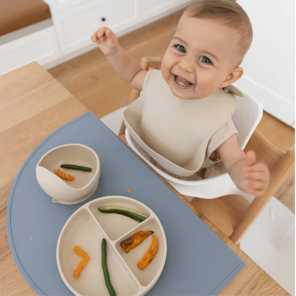 Little baby sitting at the table and eating from the Montessori First Bites Gift Set.