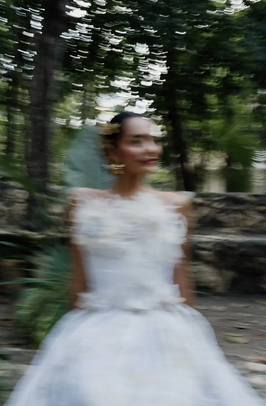 Un mannequin portant une élégante robe de mariée blanche, avec un effet de flou de mouvement pour créer une sensation de mouvement et d'élégance, dans le cadre forestier des ruines antiques de Tulum.