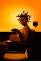 A black model with an exaggerated hairstyle is sitting on a vintage salon chair while holding a NOIRANCA handbag Amanda