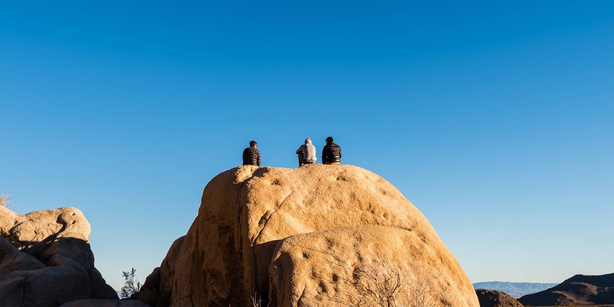Group of three guys sitting on a large rock in Joshua Tree
