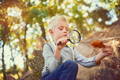 Kid playing outside and using a magnifying glass to look at a fallen leaf.