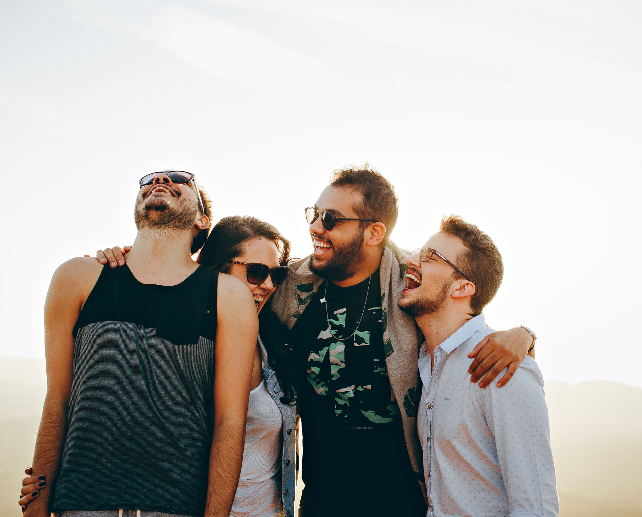 A group of friends wearing laugh loudly and holding onto eachother on top of a field.